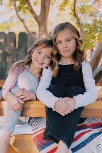 two little girls sitting on a bench in front of a tree