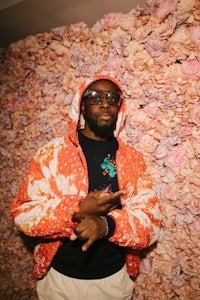 a man in an orange hoodie standing in front of a flower wall