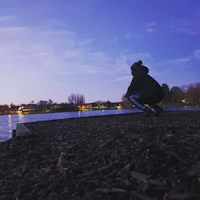 a person crouching on the edge of a lake at dusk