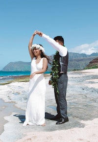 a bride and groom dancing on the beach in hawaii