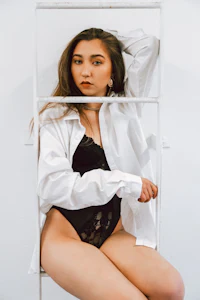 a woman in a white shirt and lingerie sitting on a ladder