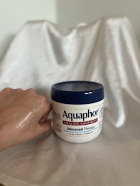 a person holding a jar of aquaphor on a white cloth