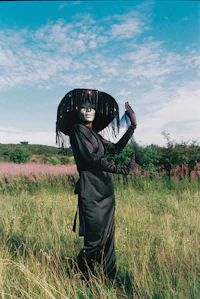 a woman in a black hat standing in a field holding a kite