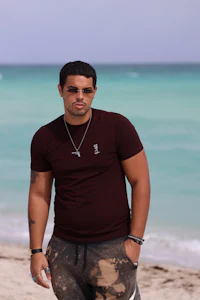 a man standing on the beach wearing a maroon t - shirt