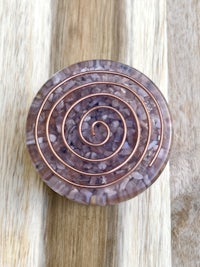 a purple and copper spiral brooch on top of a wooden table