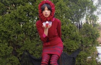 a woman in a red dress and striped stockings posing in front of bushes