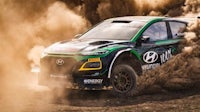 a green and black rally car driving through dirt