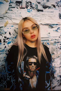 a woman wearing sunglasses and a t - shirt in front of a wall