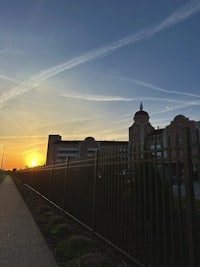 the sun is setting behind a fence