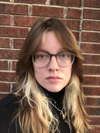 a woman in glasses is leaning against a brick wall