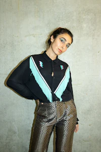 a woman is posing in front of a wall wearing a fringed shirt and pants