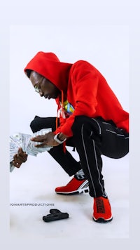 a man in a red hoodie is kneeling down and holding money