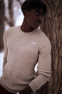 a black man in a sweater leaning against a tree