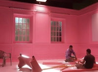 two men sitting in a room with pink walls