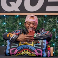 a man is holding a phone while sitting on a colorful duffle bag