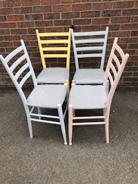 four pastel colored chairs in front of a brick wall