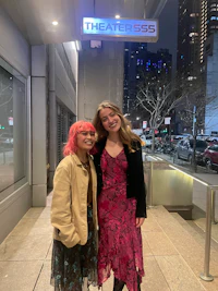 two women standing next to each other in front of a building