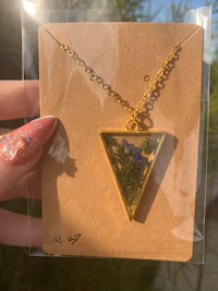 a person holding a gold triangle necklace in front of a tree