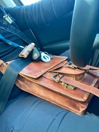 a man sitting in a car with a leather bag