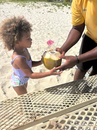 a man handing a little girl a coconut drink on the beach