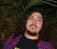 a man with long hair standing in front of palm trees