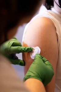 a person in a green glove is putting a patch on a person's arm