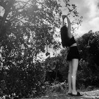 a black and white photo of a woman reaching for a tree