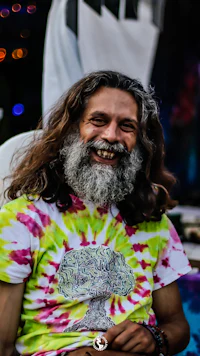 a man with long hair and a tie dye t - shirt smiling