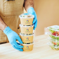 a man in blue gloves holding a stack of plastic containers