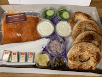 a box containing bagels, salmon, cucumbers and dips