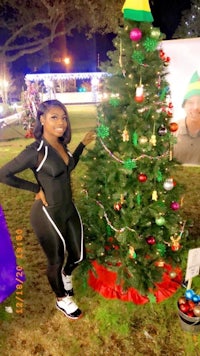 a woman is posing next to a christmas tree