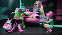 two barbie dolls sitting on a pink couch