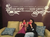 two women sitting on a couch holding cups of coffee