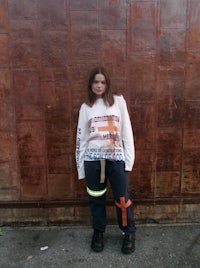 a woman wearing a sweatshirt and pants standing in front of a brick wall