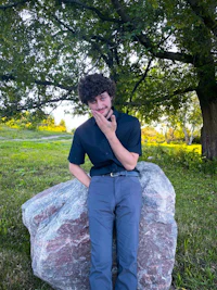 a young man sitting on a large rock