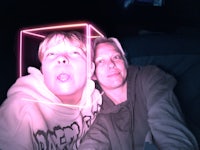 a man and a woman taking a selfie in front of a neon light