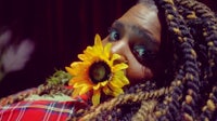 a woman with dreadlocks holding a sunflower