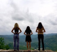 three women standing on a cliff overlooking a mountain