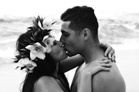 a couple kissing on the beach with flowers in their hair