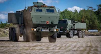 two military vehicles are driving down a dirt road