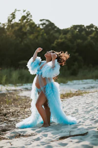 a pregnant woman in a blue dress is dancing on the beach