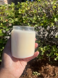 a person holding a white candle in front of bushes