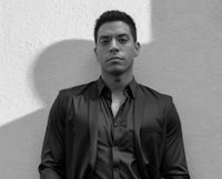 a man in a black suit leaning against a wall