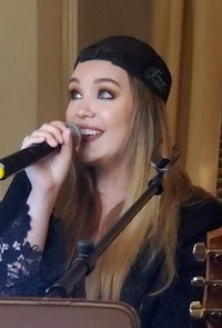 a woman singing into a microphone while holding an acoustic guitar
