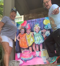 two people standing next to a painting of a birthday party