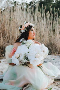 a woman is sitting on the beach holding a bouquet of flowers
