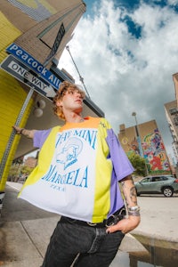 a man in a t - shirt leaning against a street sign