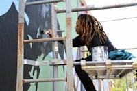 a woman with dreadlocks painting a mural