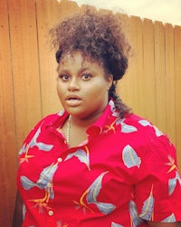 a woman in a red hawaiian shirt standing in front of a fence