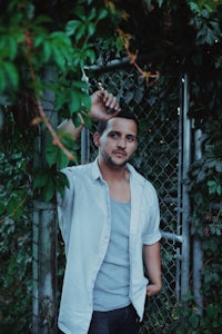 a man in a white shirt leaning against a fence